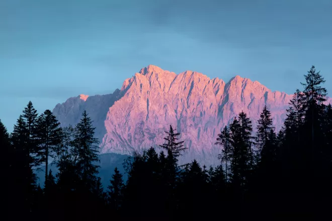 Montagne baignée dans l'Alpenglow, avec la lueur rosée ou rougeâtre du soleil couchant ou levant se reflétant sur la surface de la montagne.