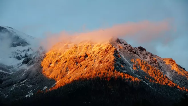 Versant de montagne pendant l'heure dorée, avec la lumière du soleil projetant une teinte chaude et dorée sur les sommets.