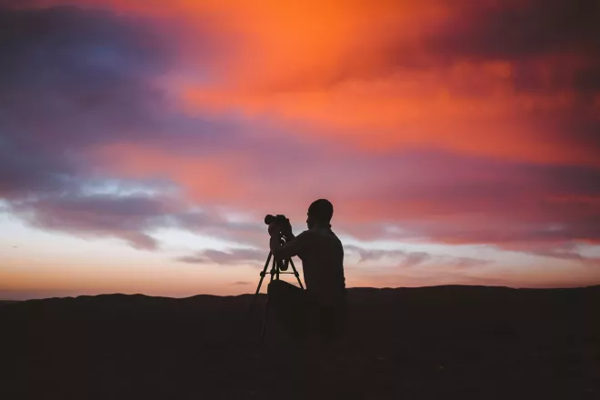 Photographe installant son appareil photo, en silhouette contre un ciel de coucher de soleil vibrant