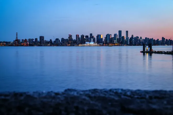 La silhouette d’une ville de l’autre côté de l’eau, sous un ciel bleu profond avec une dernière lueur rose.